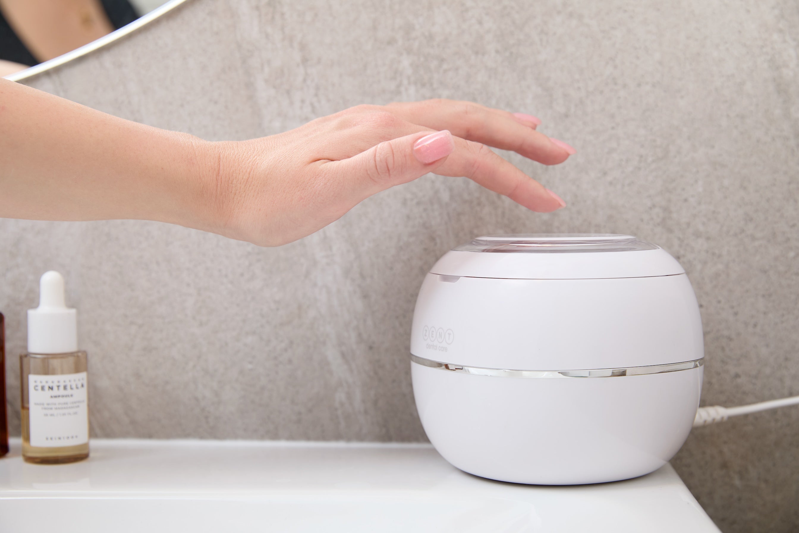 Na umywalce leży Myjka Ultradźwiękowa ZENT® Ultrasonic Cleaner, kobieca dłoń próbuje ją włączyć