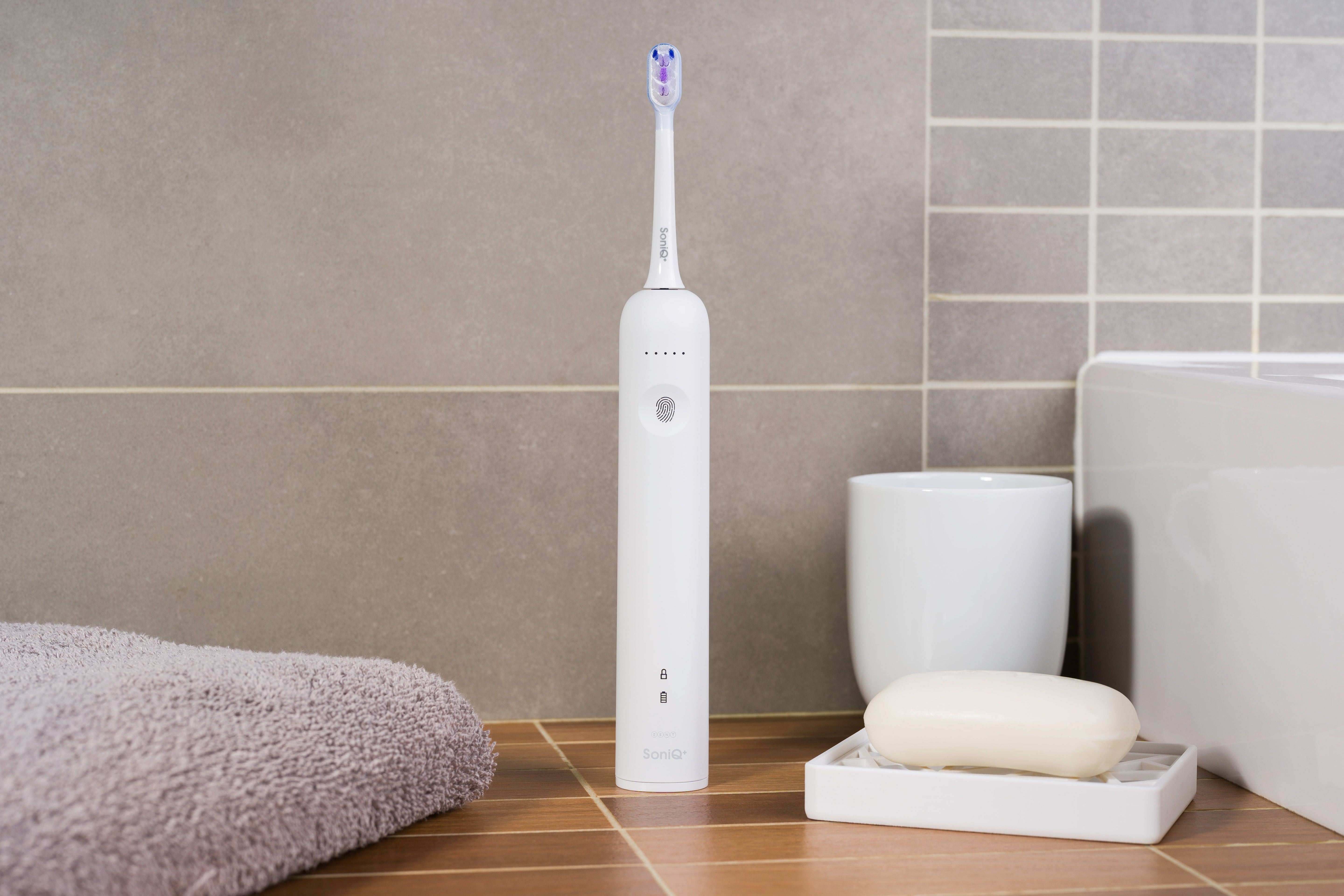 ZENT® SoniQ™ – Aktywna szczoteczka soniczna z ruchem oscylacyjnym 40° leżąca na blacie w łazience. Po lewej ręcznik, po prawej mydelniczka z mydłem, z tyłu kubek na szczoteczki, widać kawałek umywalki