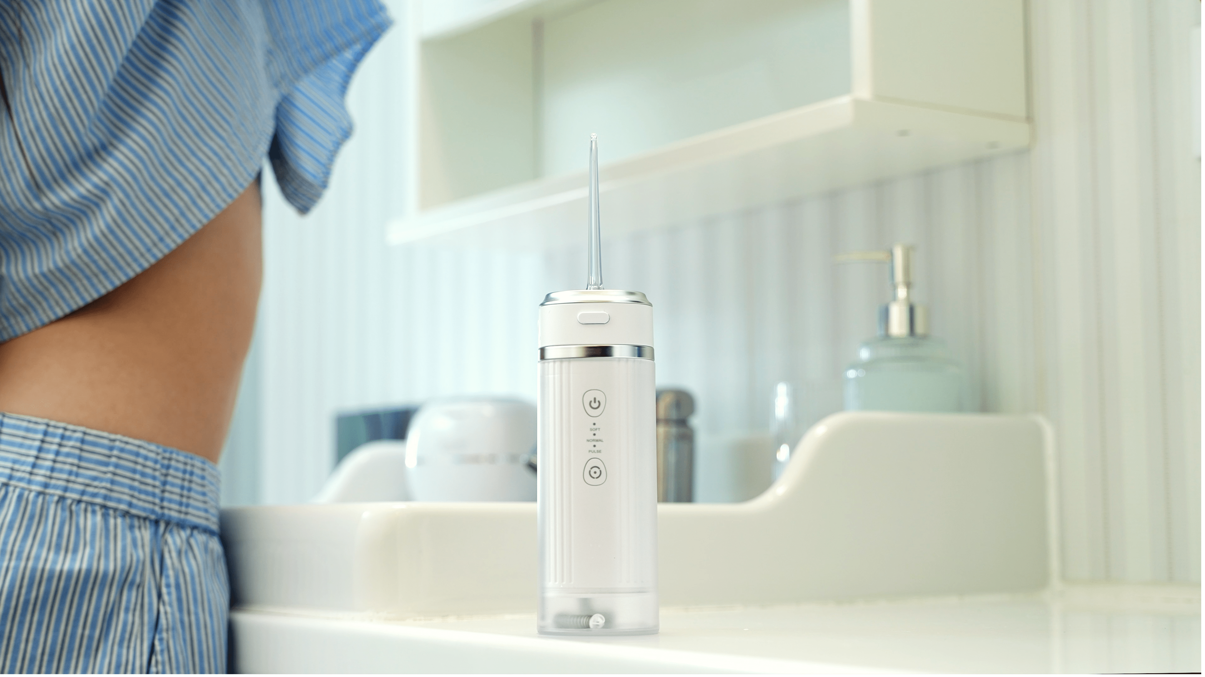 ZENT® Stream+ Irygator stomatologiczny do zębów stojący na szafce przy umywalce, w tle kobieta w piżamie