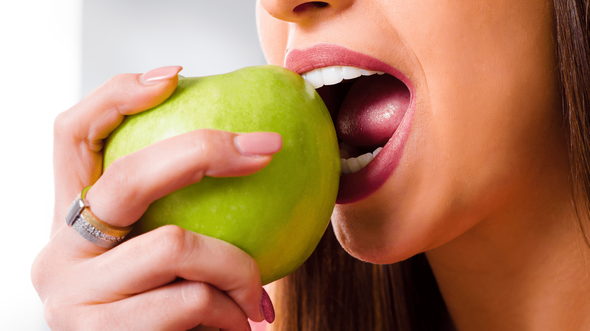 Kobieta gryzie zielone jabłko. Dieta podczas leczenia aparatem nakładowym