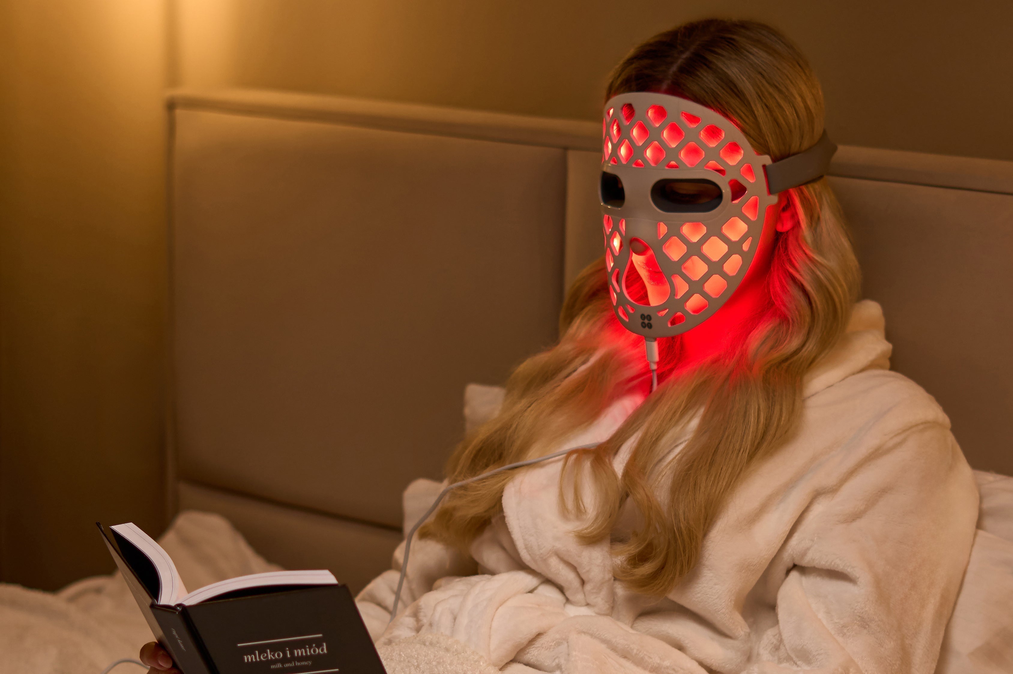 Kobieta leżąca w łóżku i czytająca książkę z maską LED ZENT® DermaLight™ na twarzy